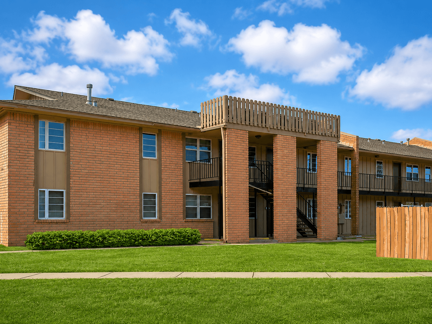 A red brick building with a balcony and a green lawn in front.